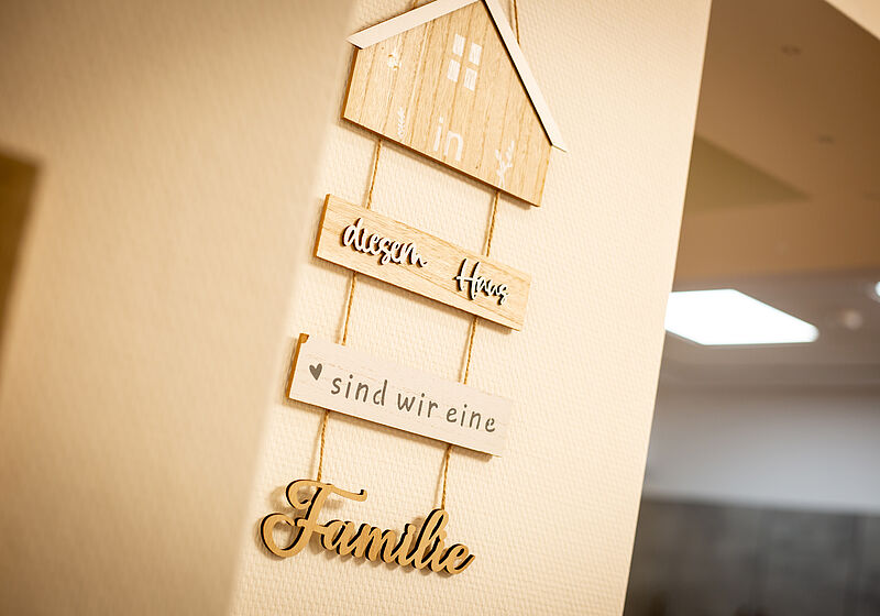 Holzdeko mit drei Schildern und dem Schriftzug "In diesem Haus sind wir eine Familie" an einer Wand.