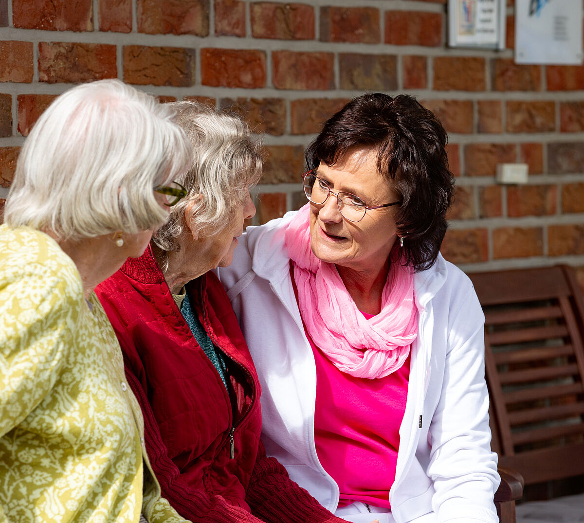 Drei Frauen sind im Gespräch auf einer Bank vor einer geklinkerten Hausmauer.
